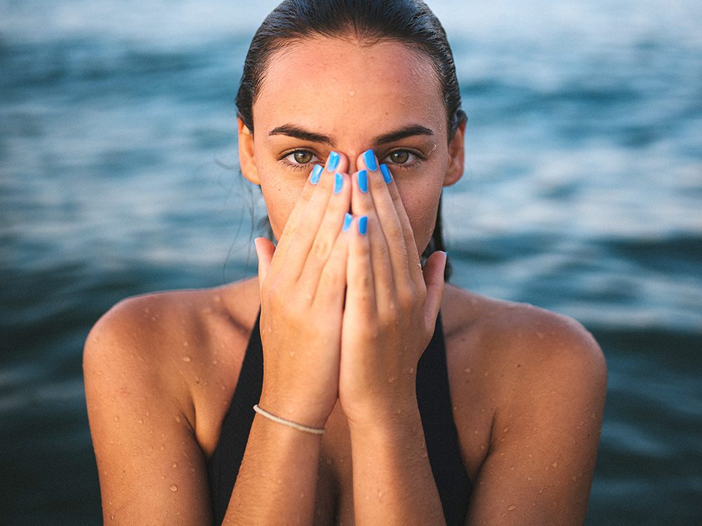 A woman with blue nails covering her face.