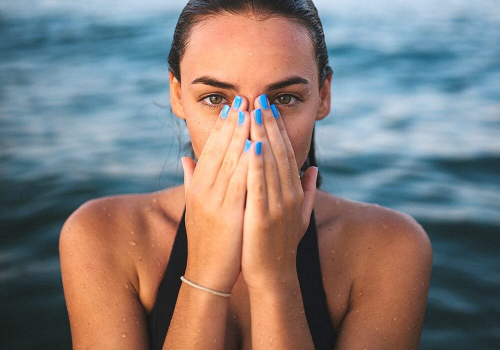 A woman with blue nails covering her face.